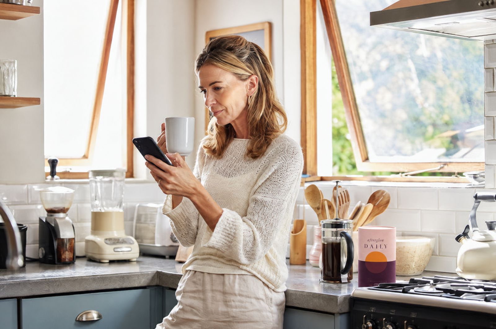 A woman checking her phone in the kitchen with coffee and Afterglow