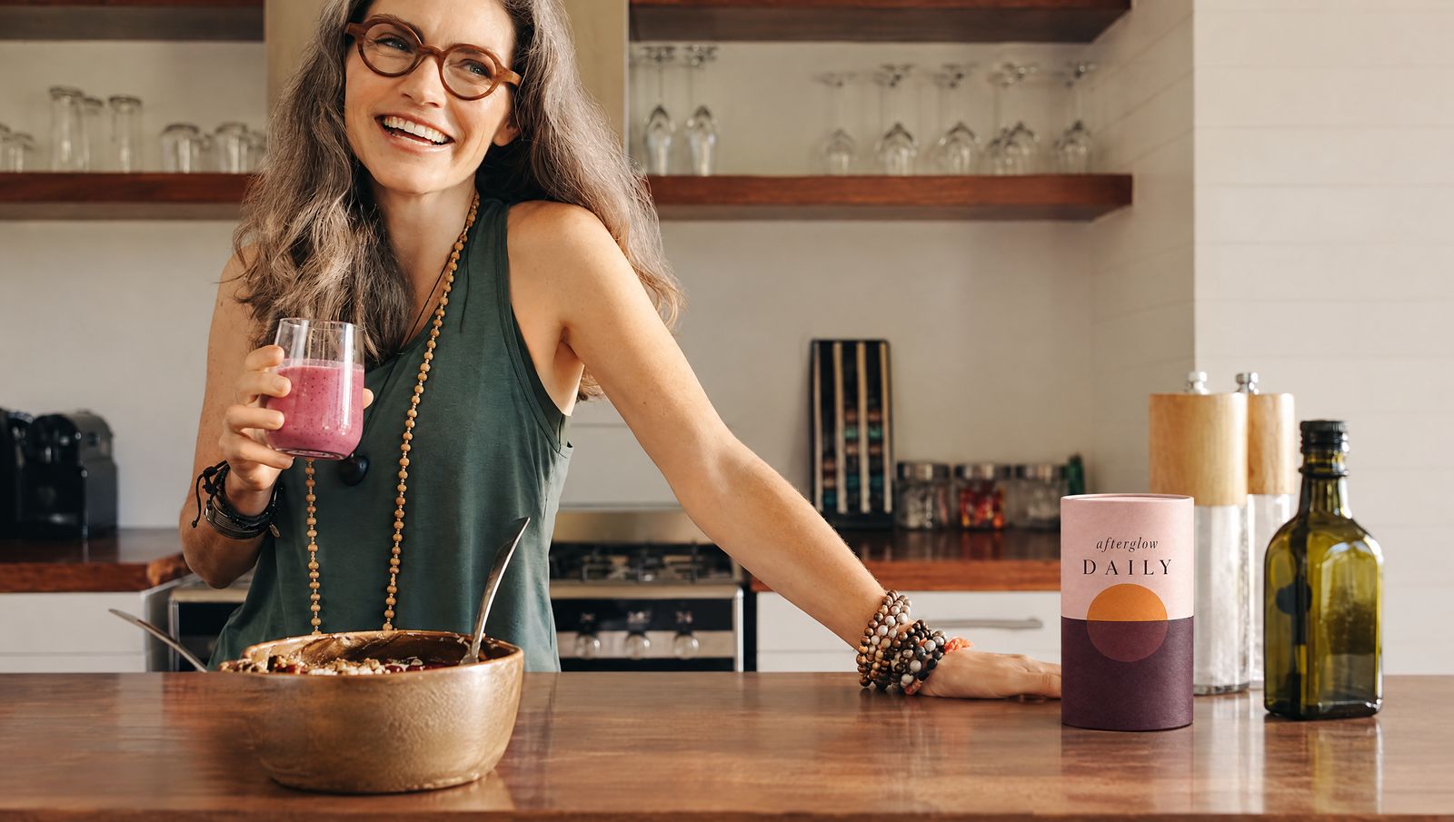 A woman with a pink smoothie in her kitchen, Afterglow on the counter