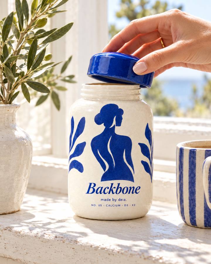 A hand lifting the glossy cobalt lid off the Backbone jar on a sunny windowsill