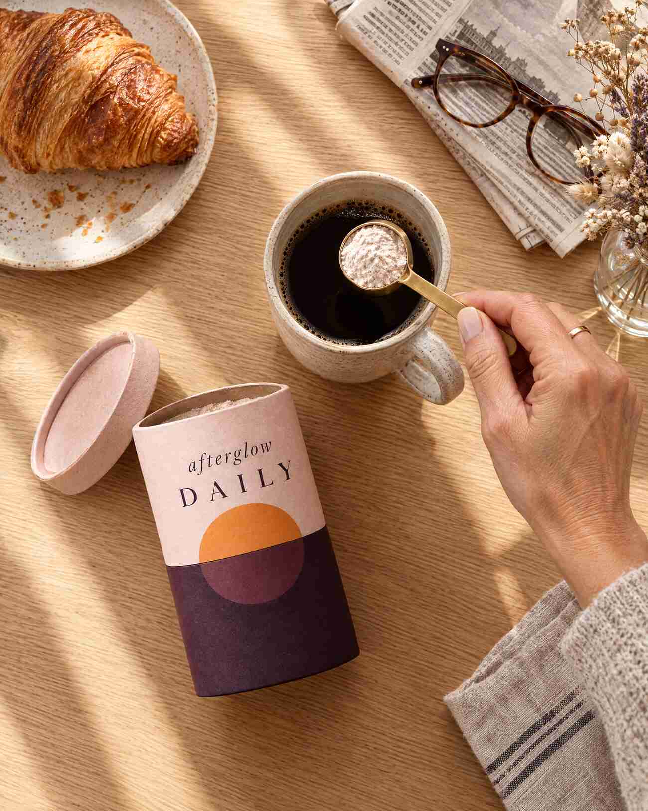 A brass scoop of afterglow DAILY over a mug of black coffee