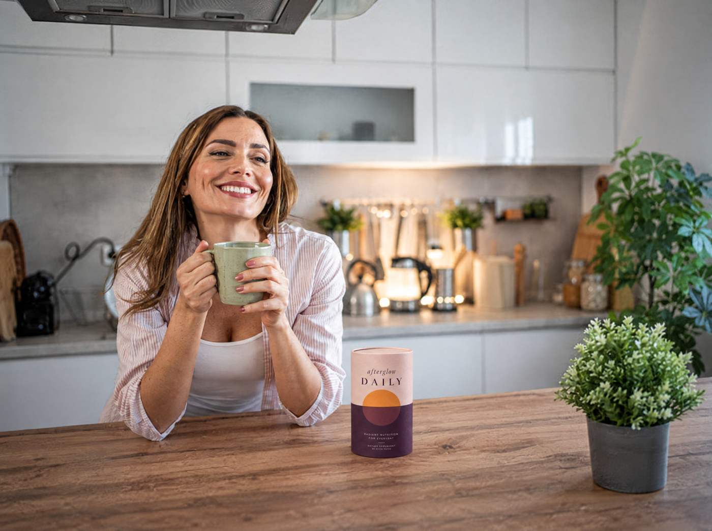 A smiling woman holding a mug at her kitchen counter, the Afterglow tub beside her