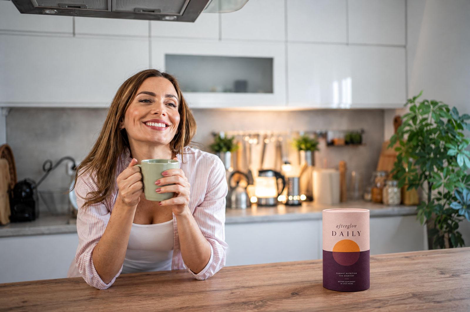 A woman smiling over her mug at the kitchen counter, Afterglow beside her