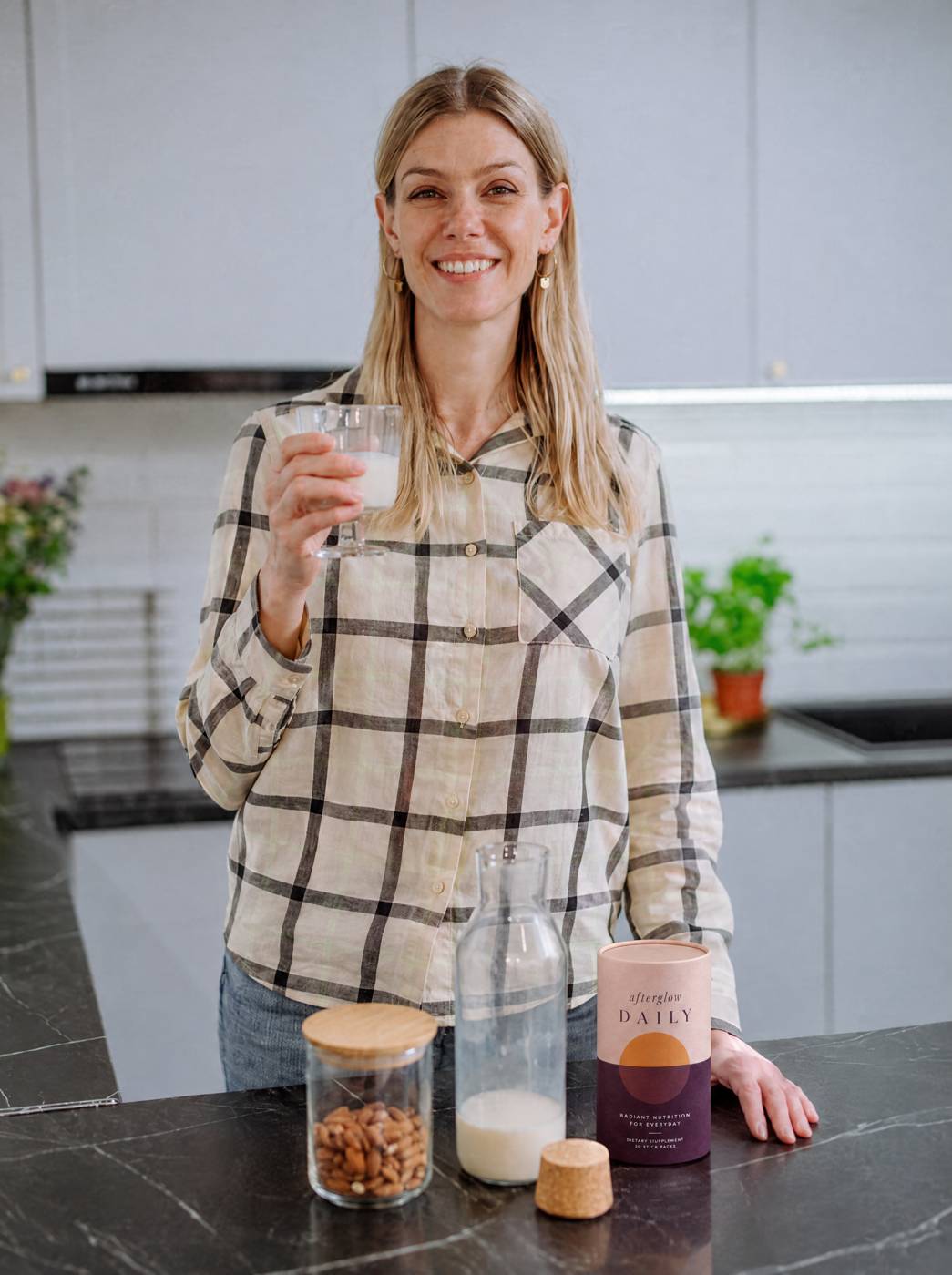 Woman with a glass of almond milk and the afterglow DAILY tub on her counter